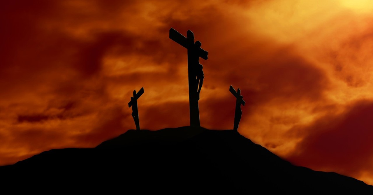 Silhouette of three crosses with men on them at sunset