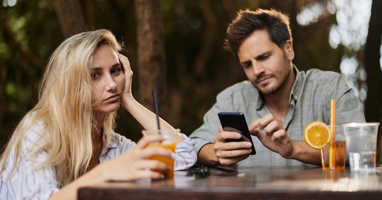 Married couple bored on date night at restaurant husband on phone ignoring wife