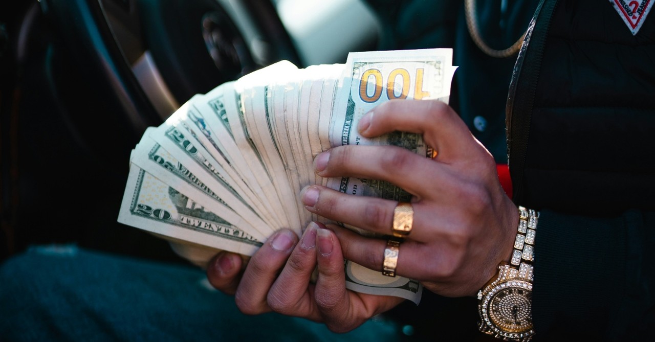 A wealthy man with gold rings and jeweled watch holding fanned out dollar bills