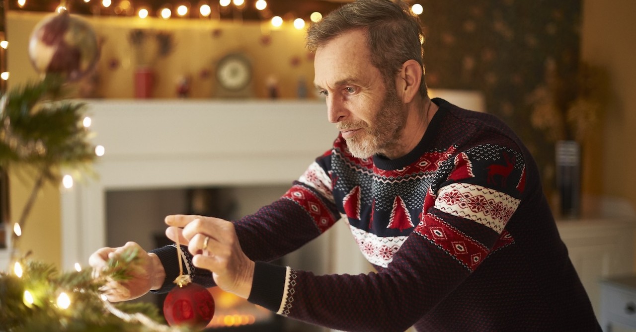 Senior man alone holidays decorating christmas tree in sweater