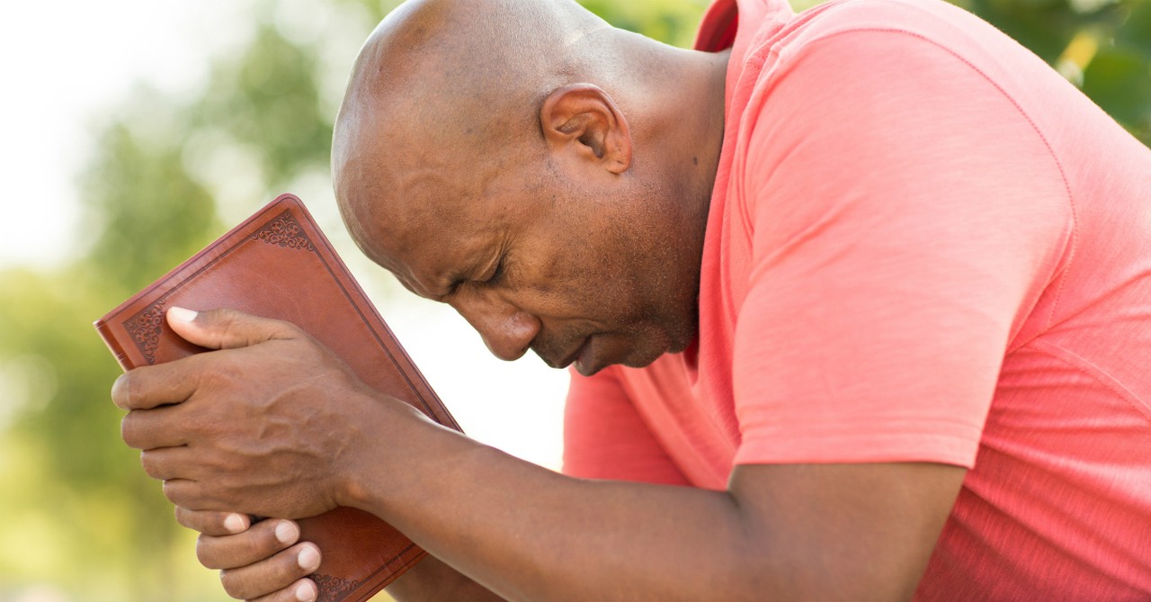 man praying holding bible eyes closed